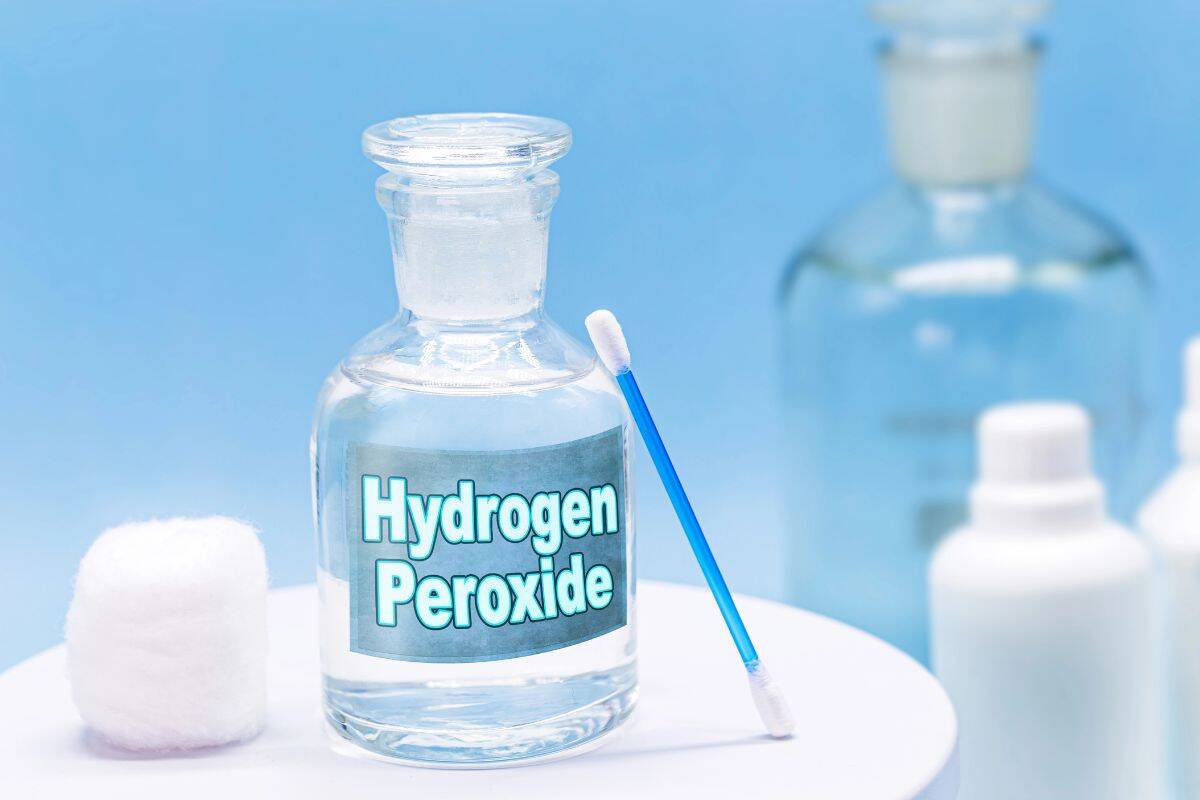 A bottle of hydrogen peroxide with cotton balls and a swab on a white surface.