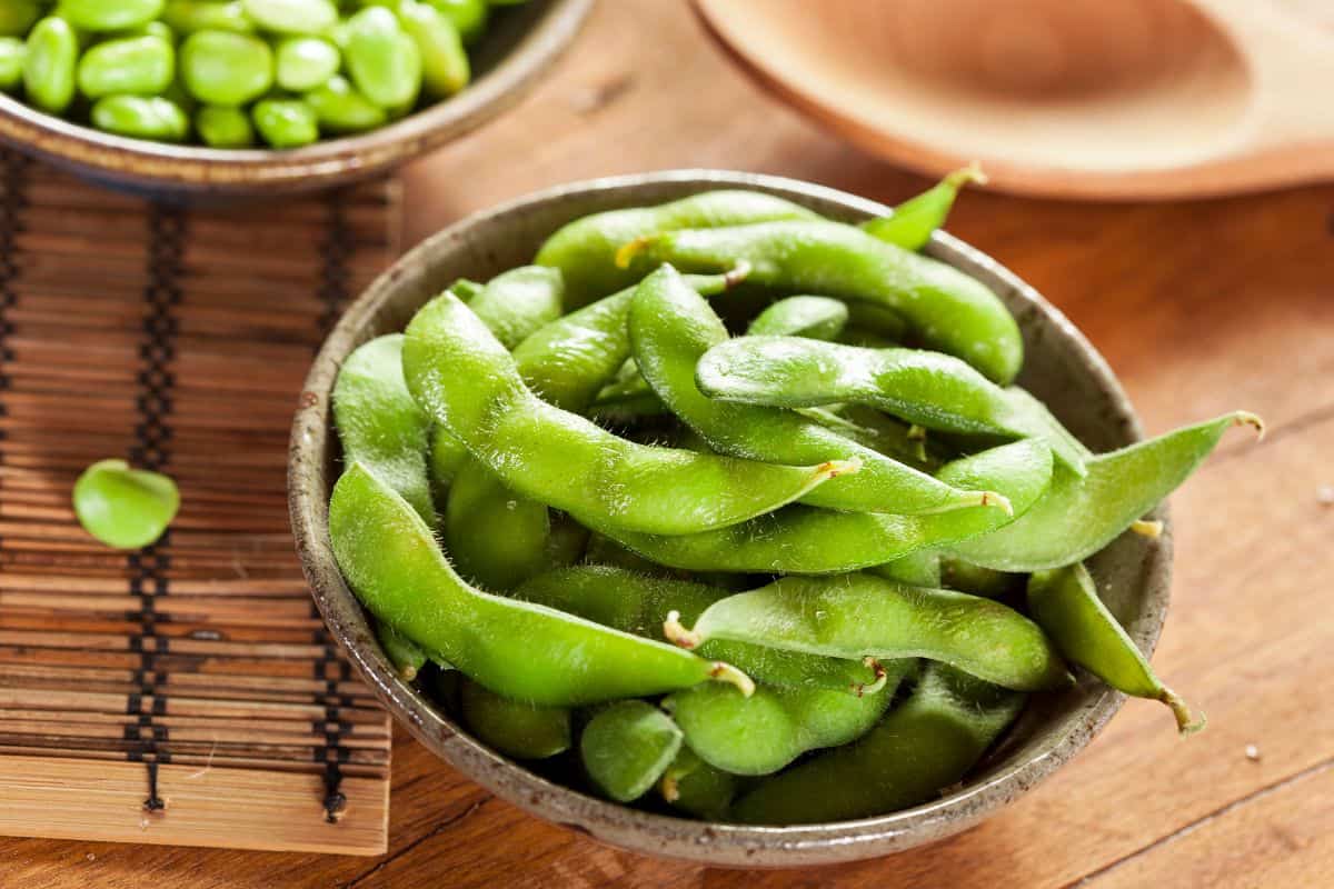 Green edamame pods in a small bowl on a wooden table.