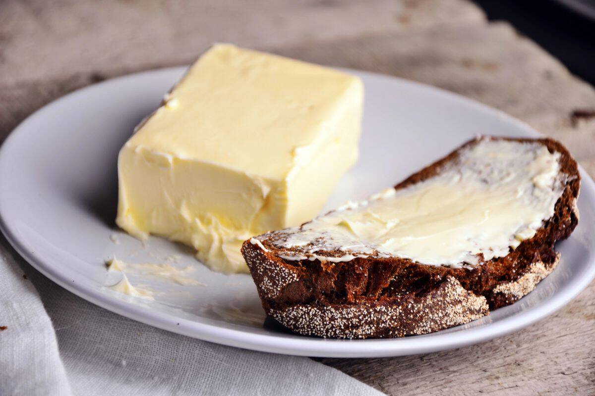 Stick of butter and buttered bread on a white plate.
