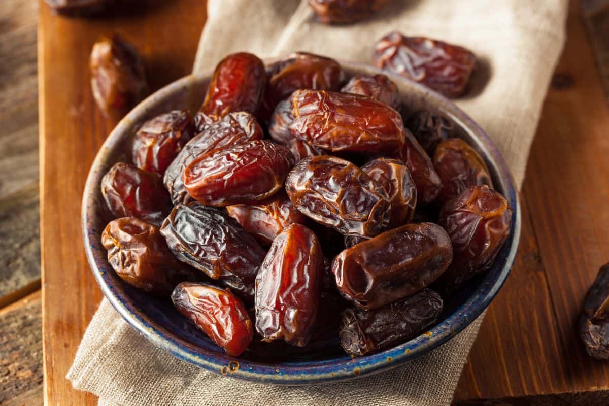 Bowl filled with dried dates on a wooden table.