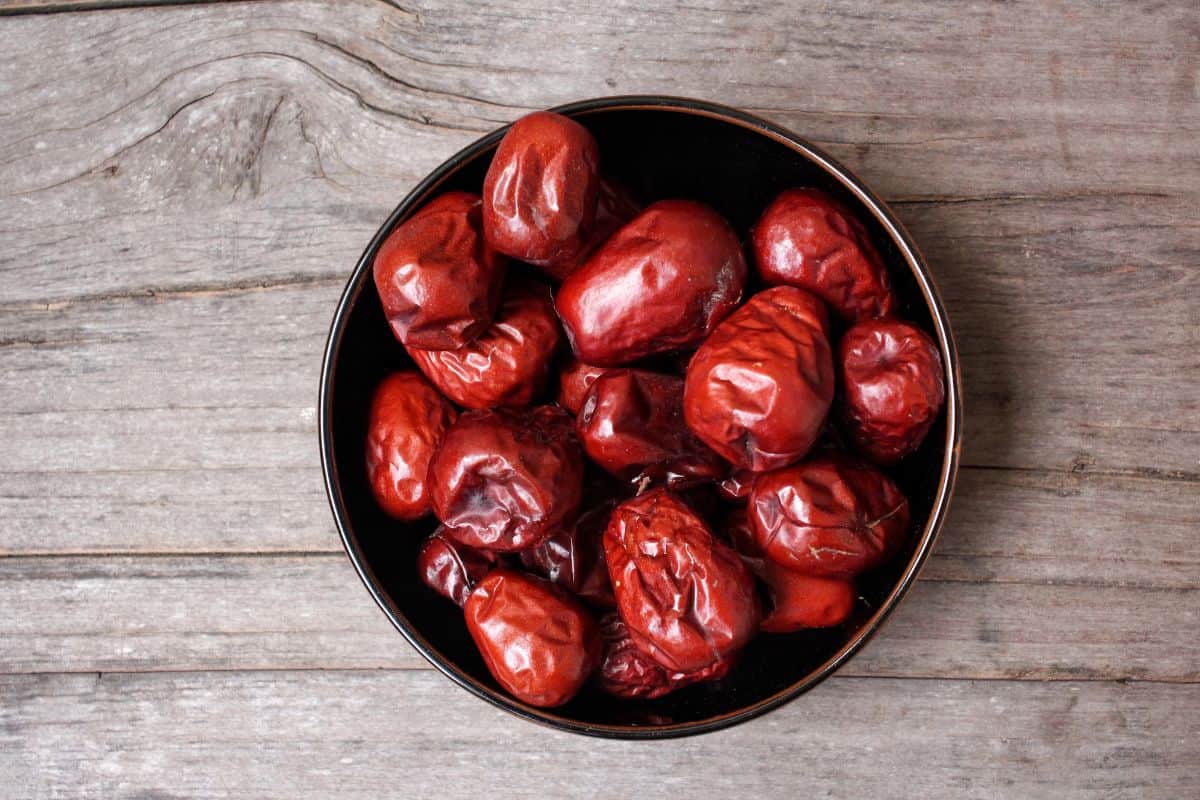 Bowl of red dates on a rustic wooden surface.