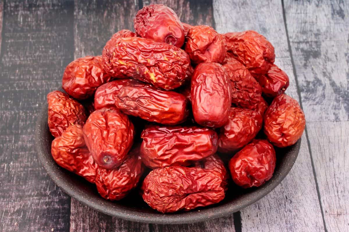 Bowl filled with dried red dates on a wooden table.