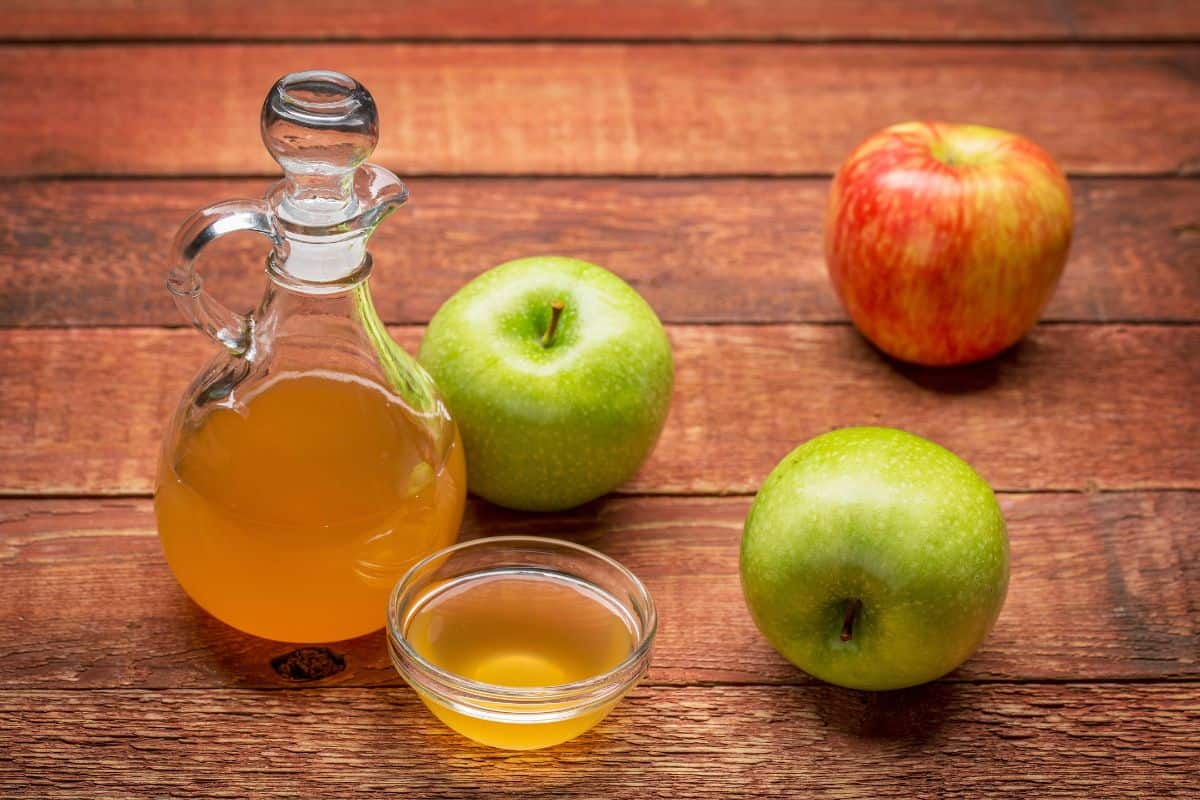 Apple cider vinegar with fresh apples on a wooden table.