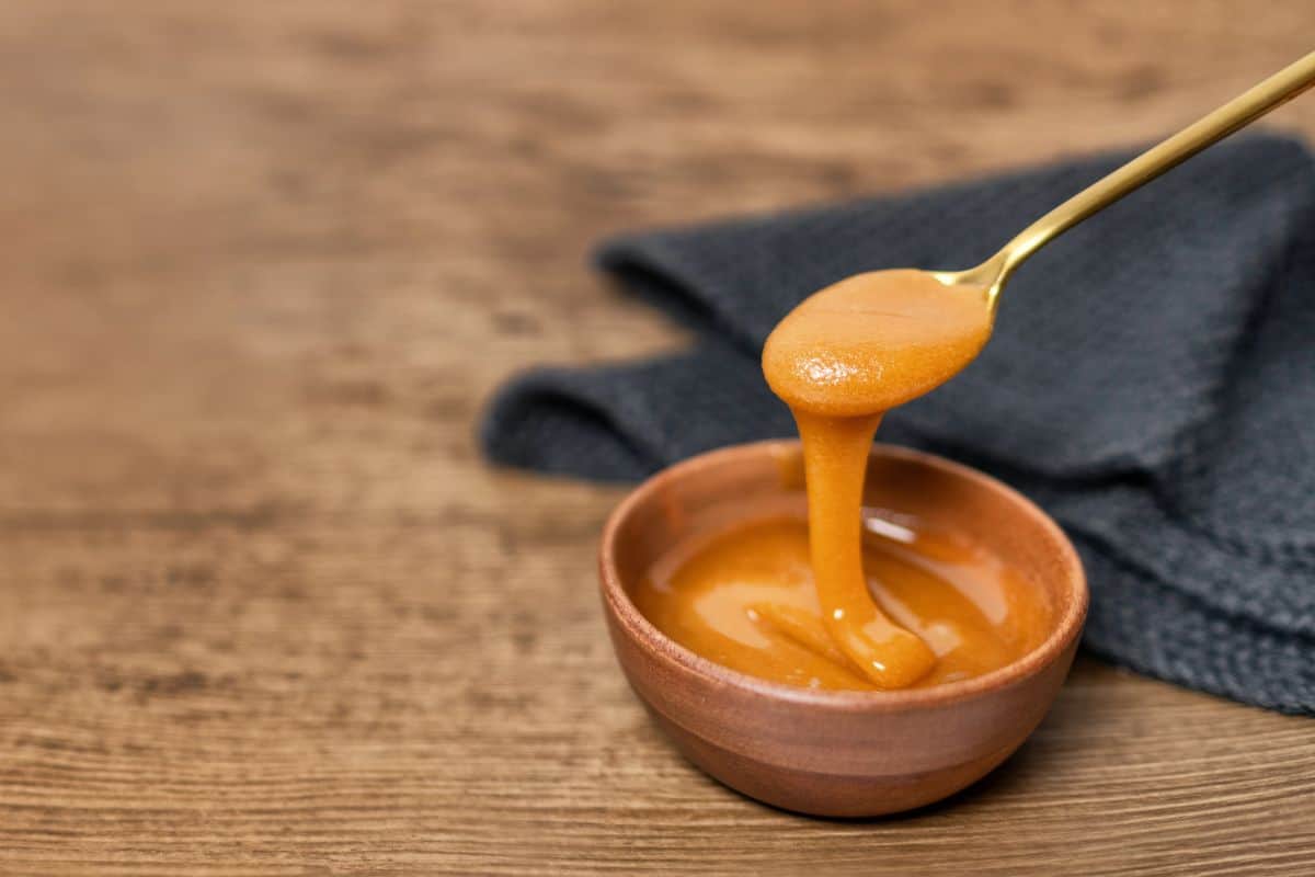 Spoon pouring honey into a small wooden bowl.