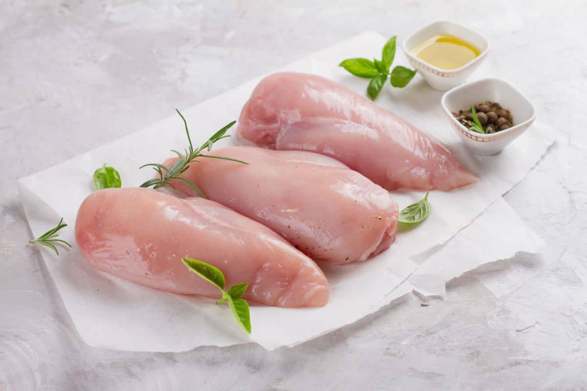 Raw chicken breasts arranged on parchment paper with fresh herbs.