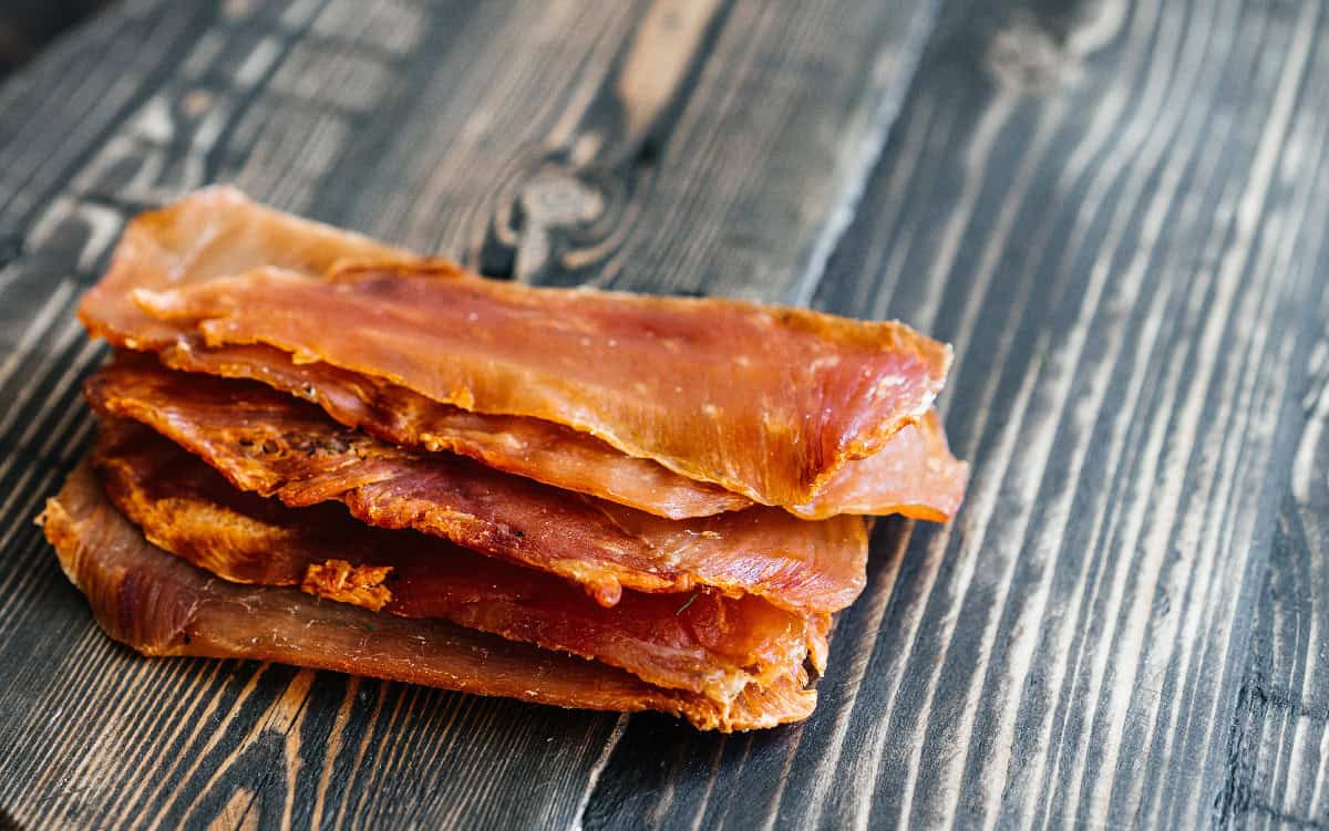 Stack of homemade dog jerky strips arranged on a rustic wooden table, highlighting their chewy texture.