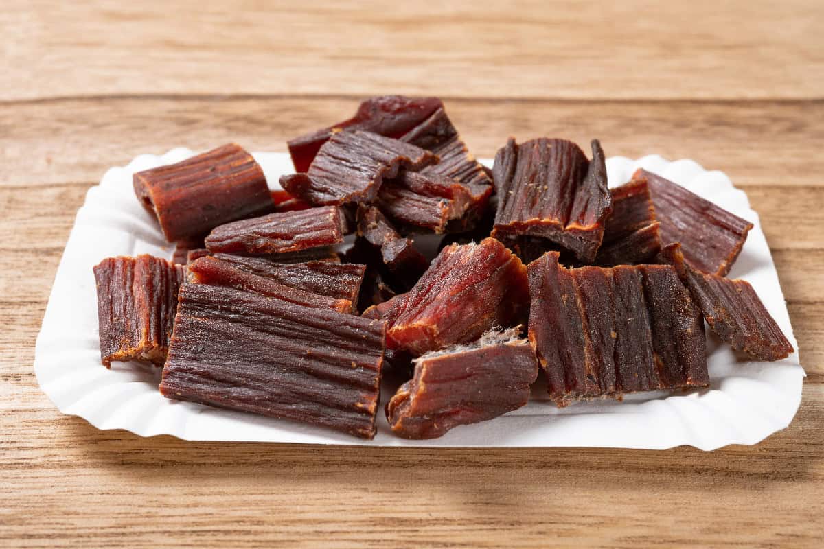 Bite-sized dog jerky treats arranged on a white paper tray over a wooden surface, ready for rewarding dogs.