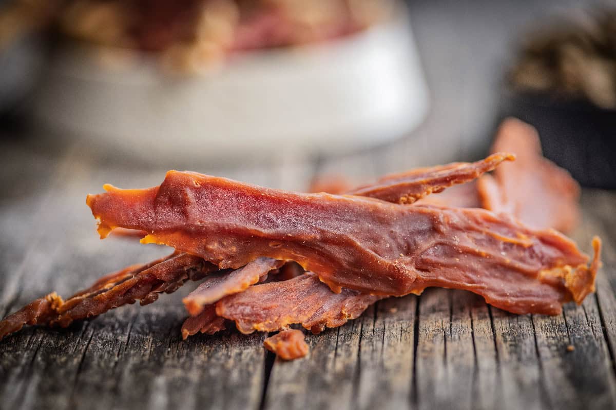 Close-up of thin homemade dog jerky strips stacked on a rustic wooden table with a soft blurred background.
