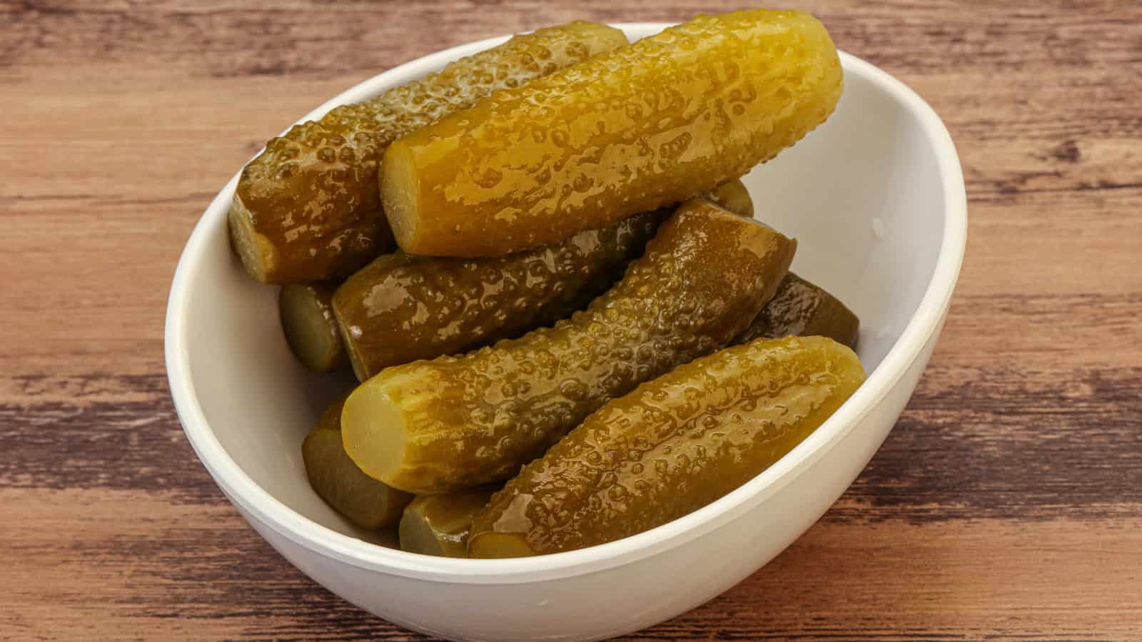 Bowl of whole pickles on a wooden table.